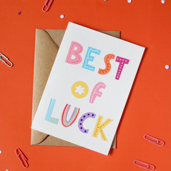 A white greeting card with 'Best of Luck' text on an orange background with decorative elements.