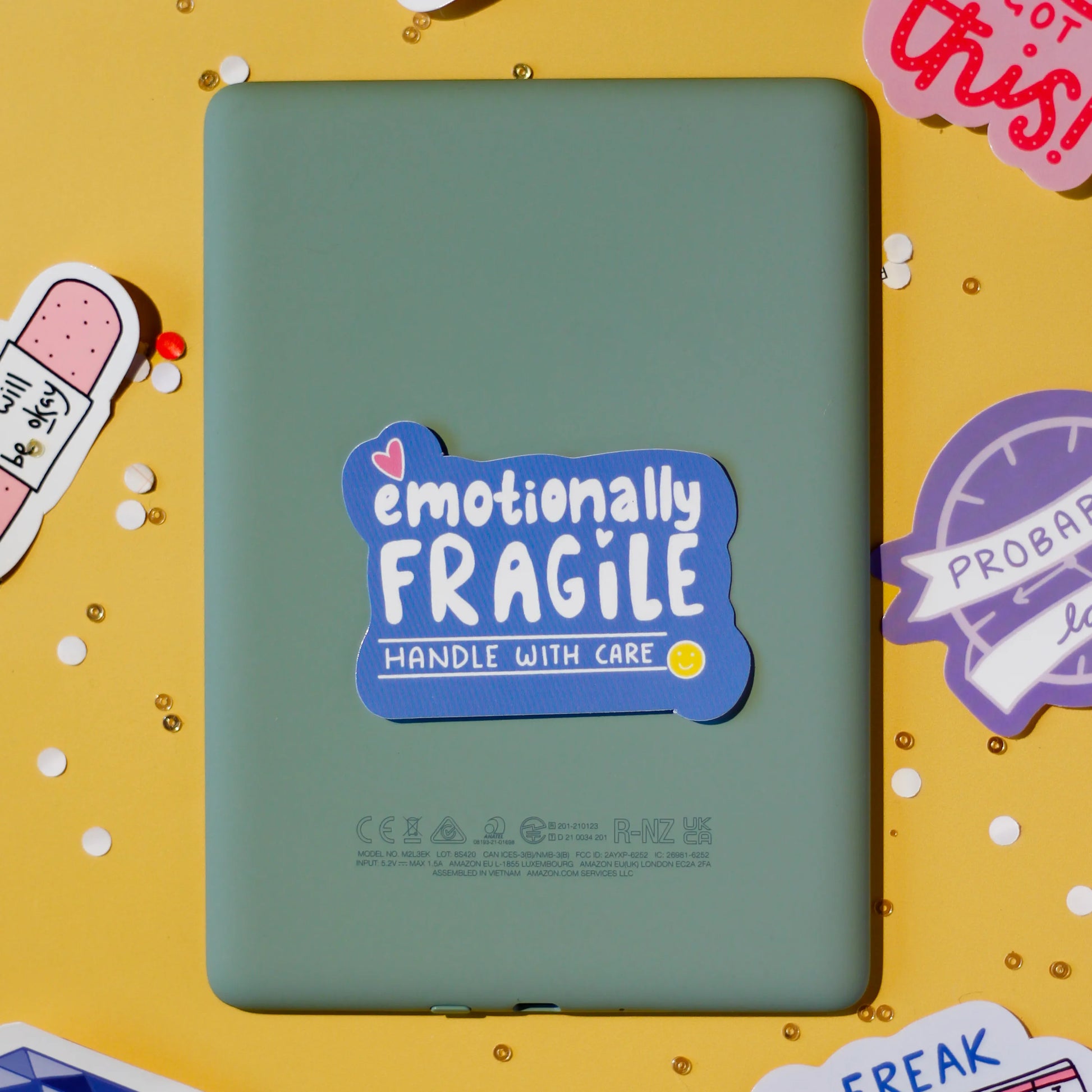 a 'emotionally fragile handle with care' sticker on a yellow background with confetti.
