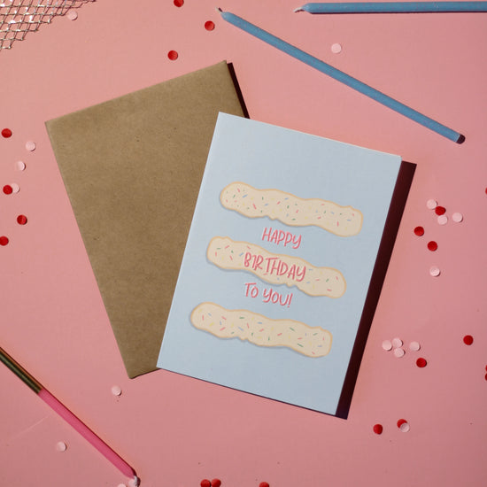 A blue card with frosting and 'Happy Birthday To You!' text on a light pink background with confetti.