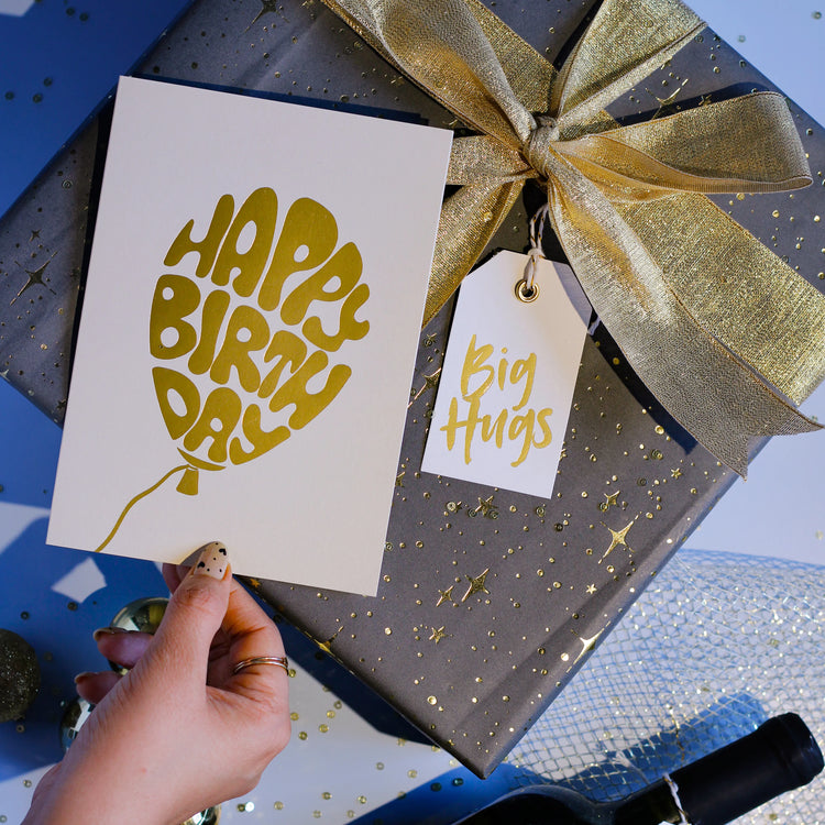 Gift box with gold ribbon and 'Happy Birthday Golden Balloon' card, held by a hand.