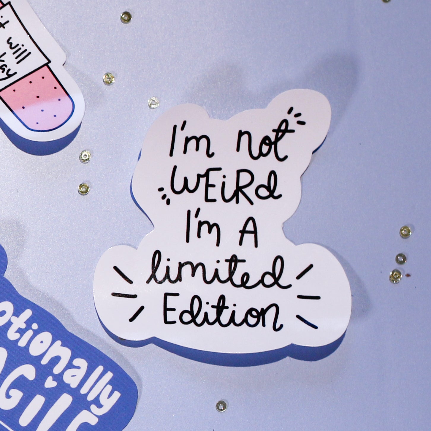 A close-up of our 'I'm not Weird I'm a limited Edition' sticker on a light blue background with decorative elements.