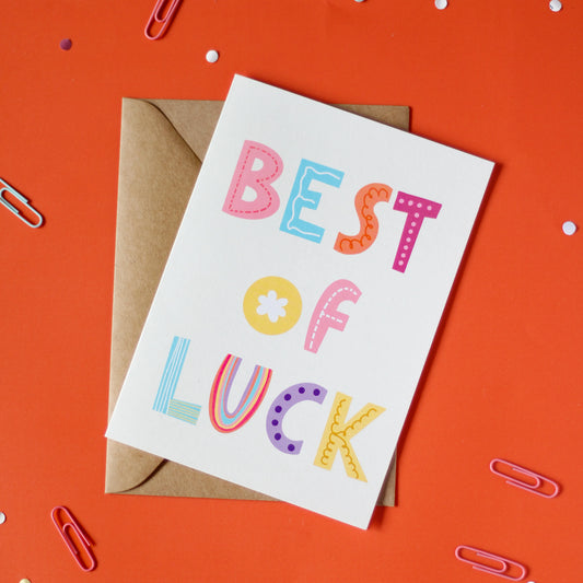 A white greeting card with 'Best of Luck' text on an orange background with decorative elements.