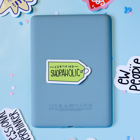 'Certified Shopaholic' on a light blue background with decorative elements.