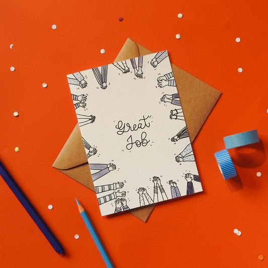 A white greeting card with 'Great Job' text and hand illustrations, accompanied by a brown envelope against a red background with stationery items.