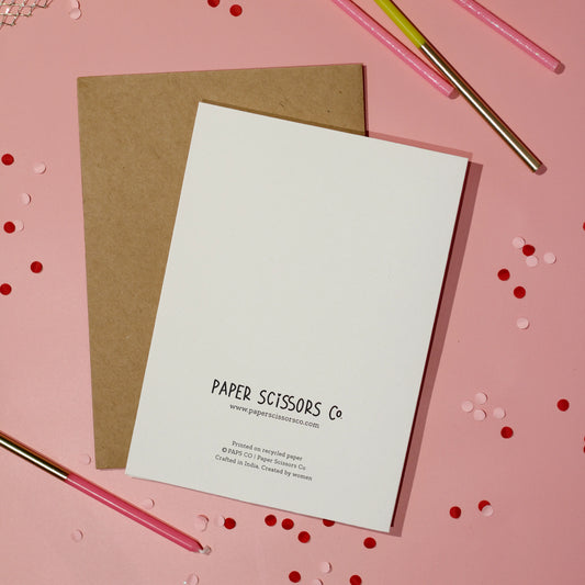 A white greeting card back cover highlighting 'Paper Scissors Co.' text on a light pink background with confetti.