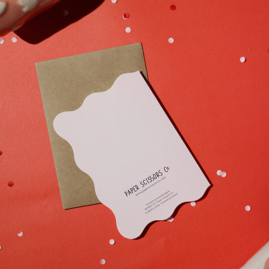 A white die-cut card with 'Paper Scissors Co.' accompanied by a brown envelope on a red background with decorative elements.