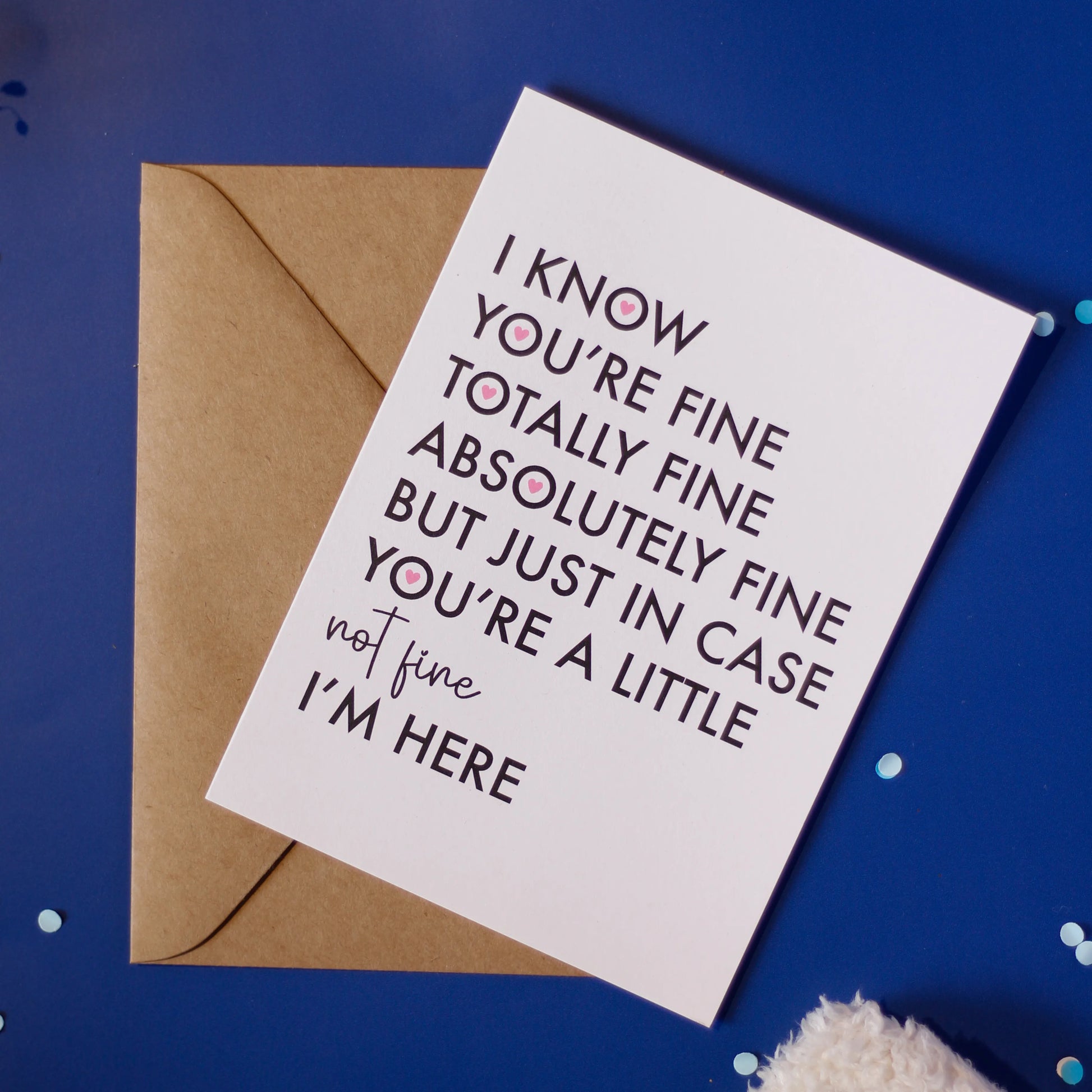 A white greeting card with "I know you're fine totally absolutely fine but just in case you're a little not fine I am here' and an envelope on a dark blue background