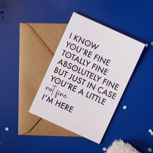A white greeting card with "I know you're fine totally absolutely fine but just in case you're a little not fine I am here' and an envelope on a dark blue background