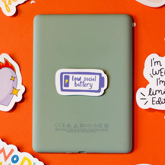 A 'Low Social Battery' sticker on an orange background with decorative elements.