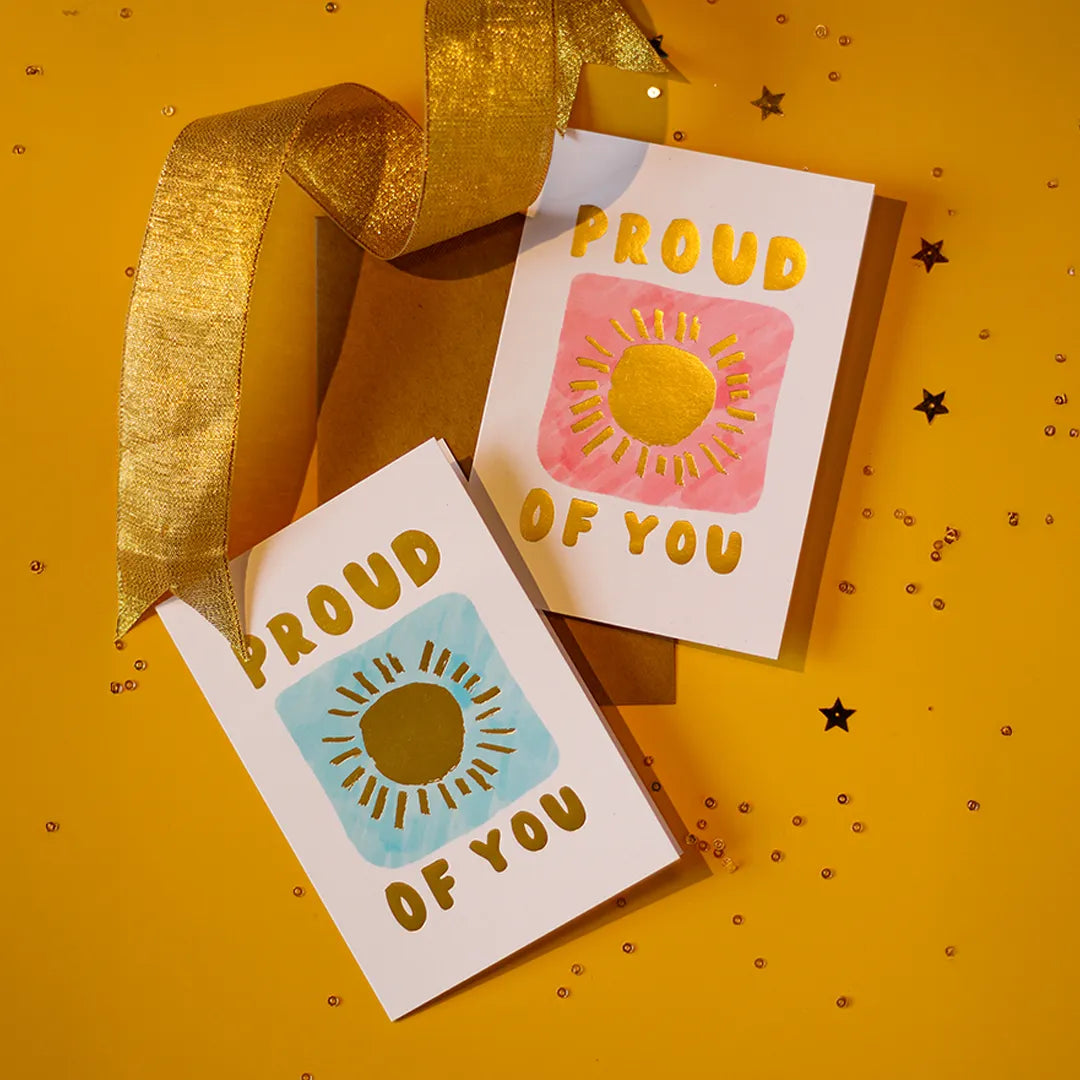 Two colour variation 'Proud of You' cards with colourful sun designs on a yellow background with a gold ribbon.