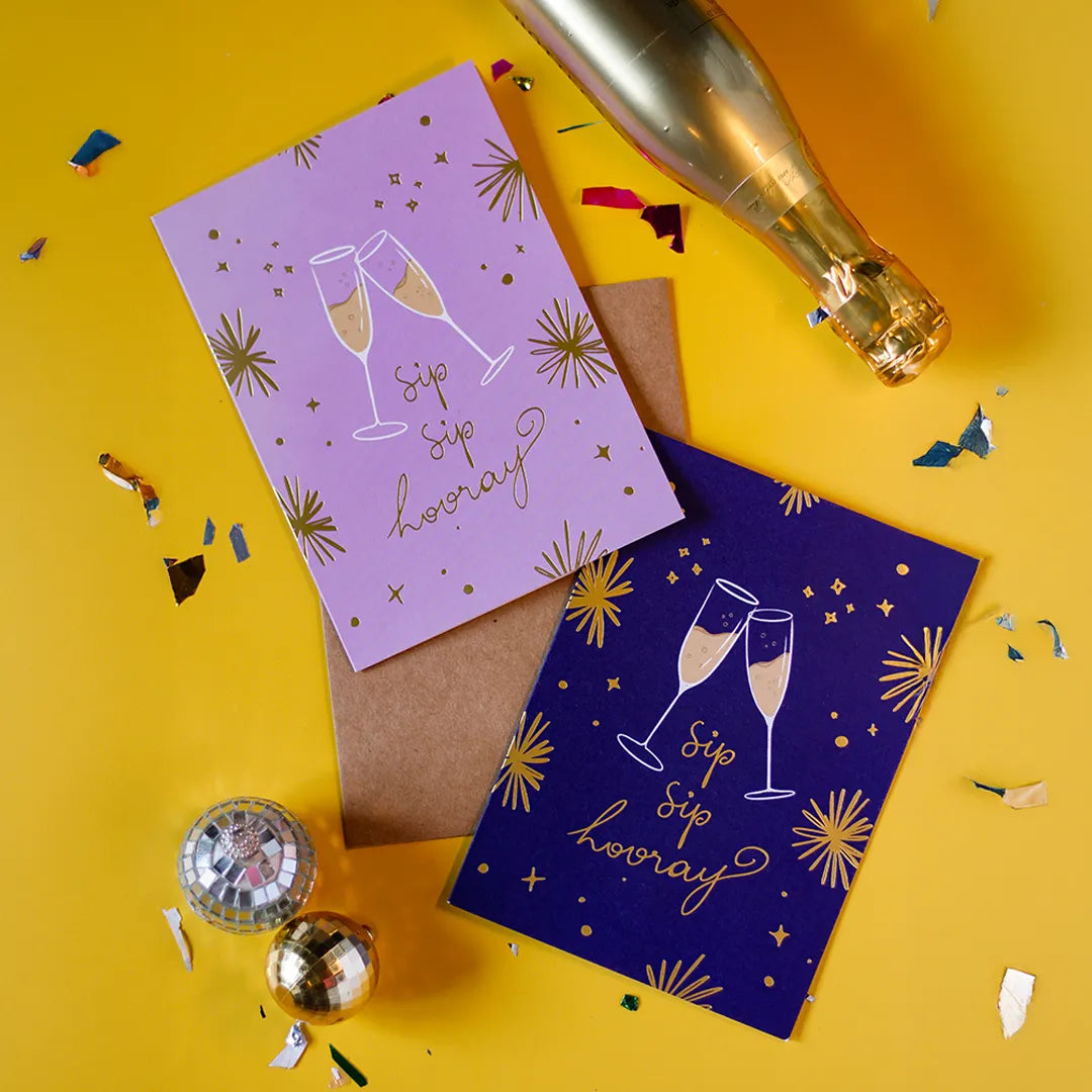 Two colour variations on our Sip Sip Hooray greeting cards with champagne illustrations on a yellow background with confetti and a champagne bottle.
