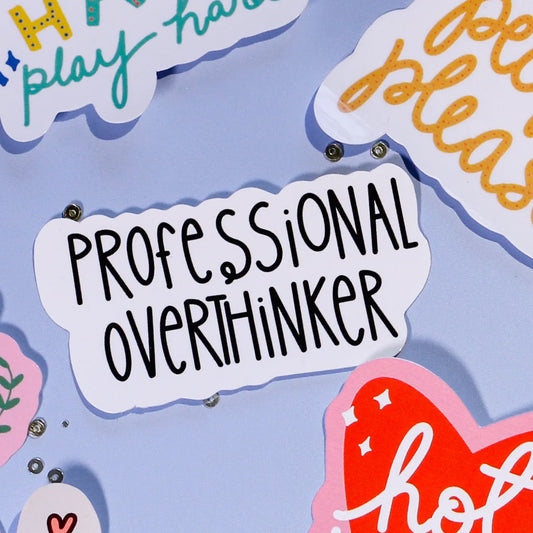 A close-up of our 'Professional Overthinker' a white and black sticker on a light blue background.