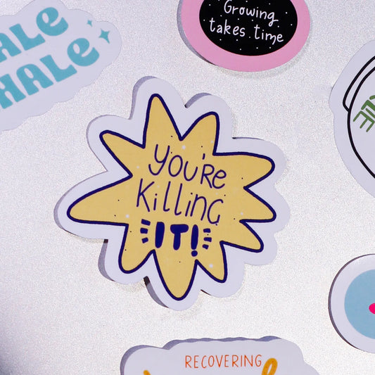 A close-up of our sticker with 'You're Killing It!' text on laptop background with our other stickers.