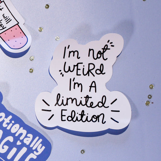 A close-up of our 'I'm not Weird I'm a limited Edition' sticker on a light blue background with decorative elements.